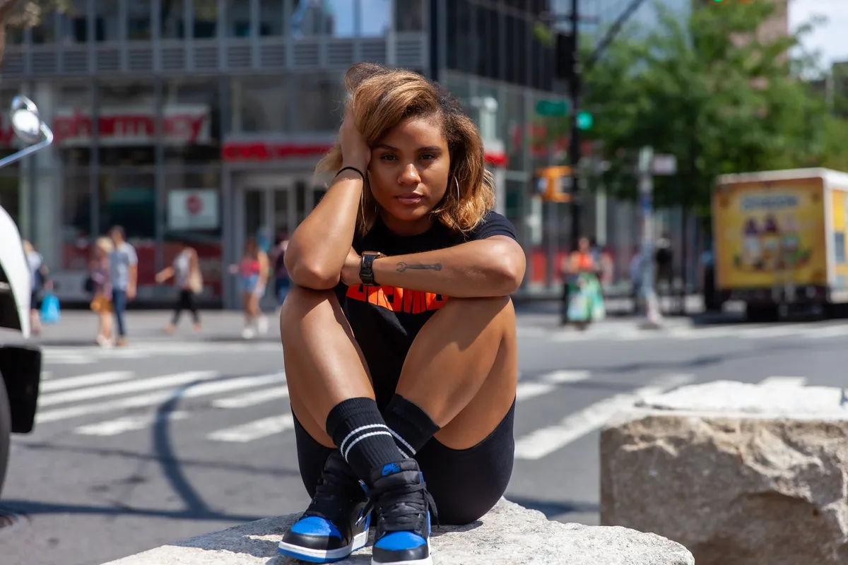 A woman sits on a granite block at a city intersection, hugging her knees
