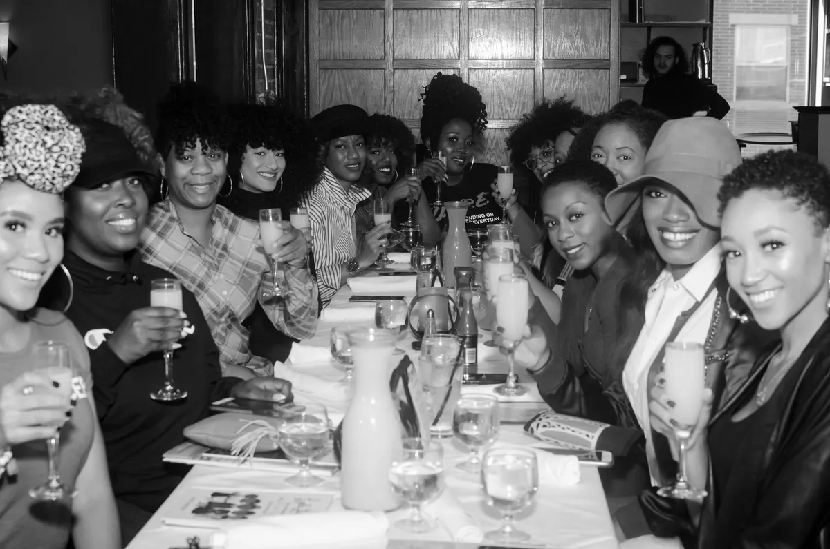 Black-and-white group photo of women raising mimosas around a long brunch table