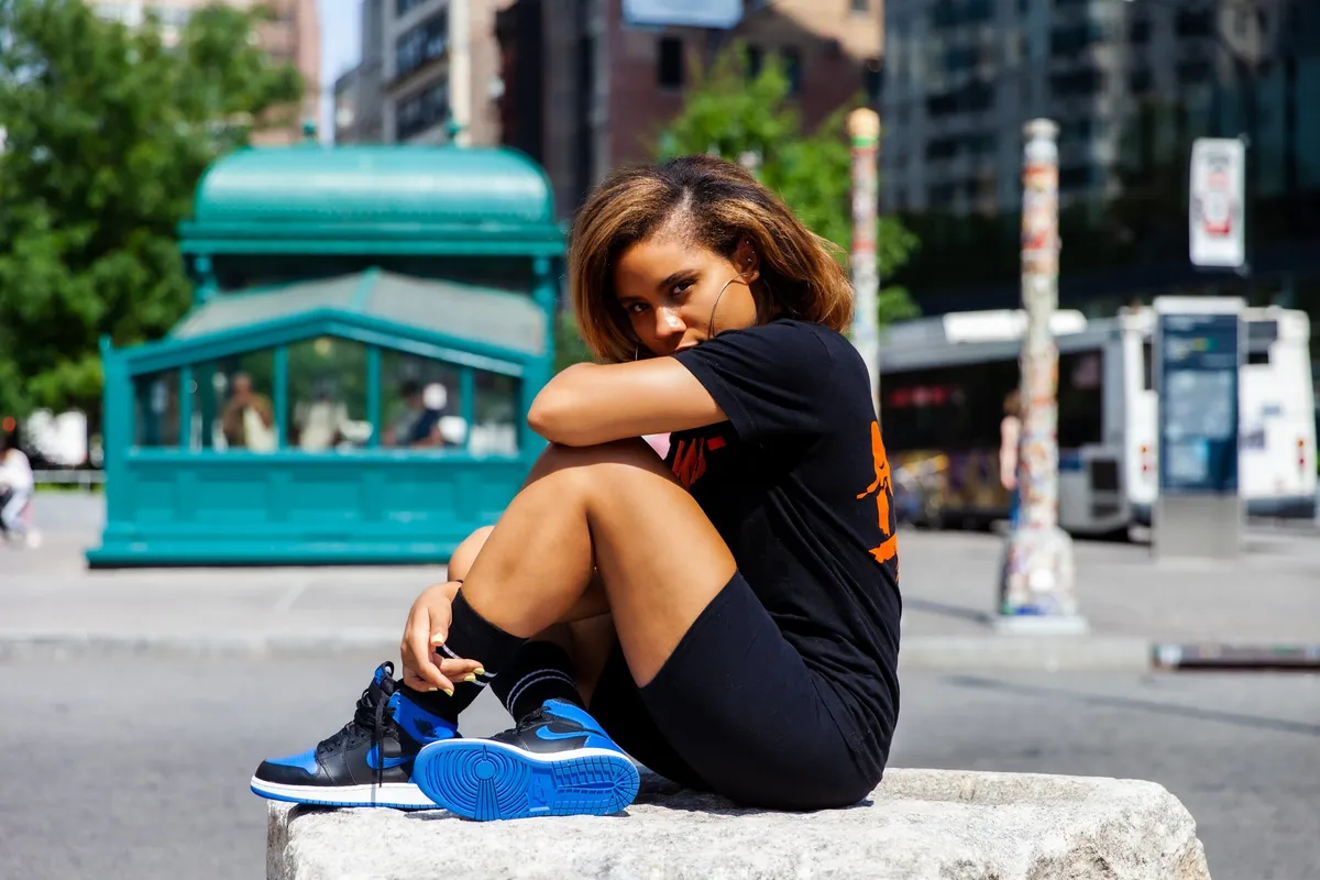 A woman perched on a granite block rests her head on her arm beside a teal subway entrance