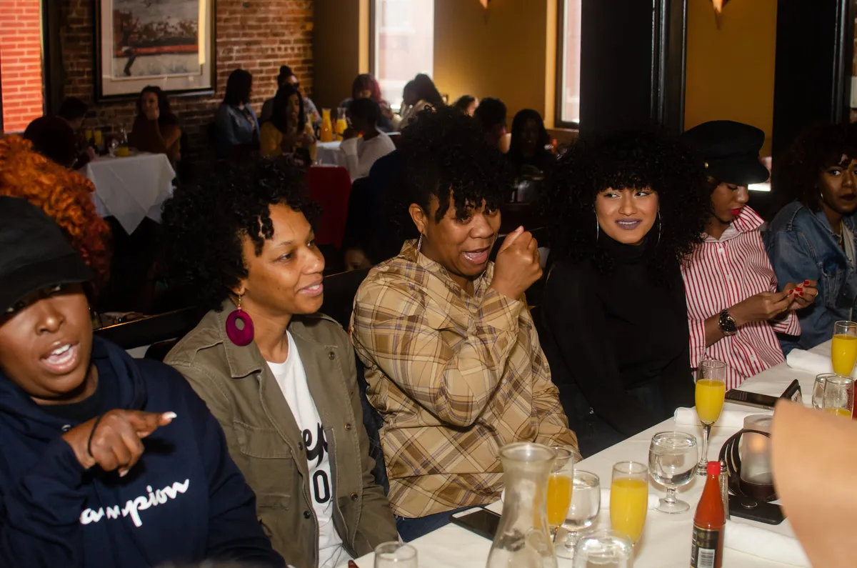 A crowded brunch table of women chatting and laughing in a warm restaurant