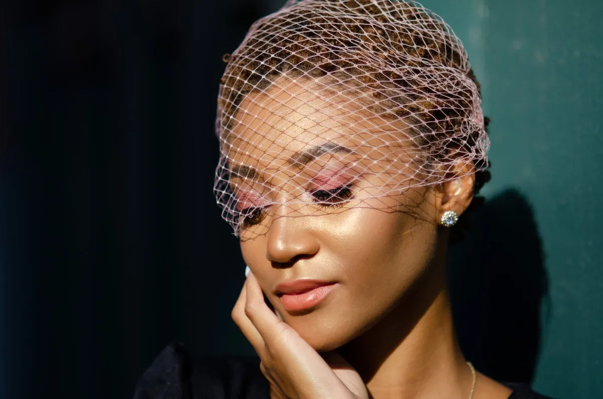 A woman in a birdcage veil looks down with her eyes closed in warm side light