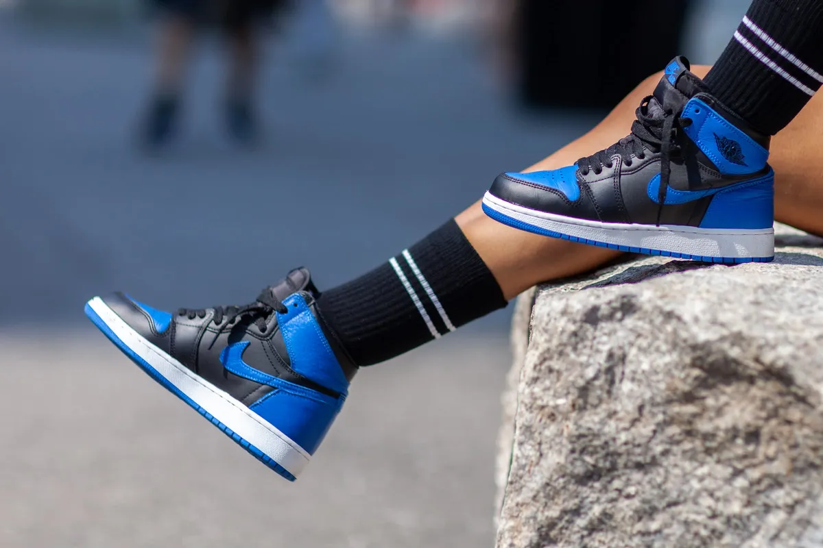 Close-up of royal blue and black high-top sneakers and striped socks resting on stone