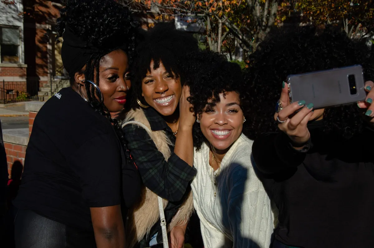 A group of women with natural hair take a selfie together outdoors