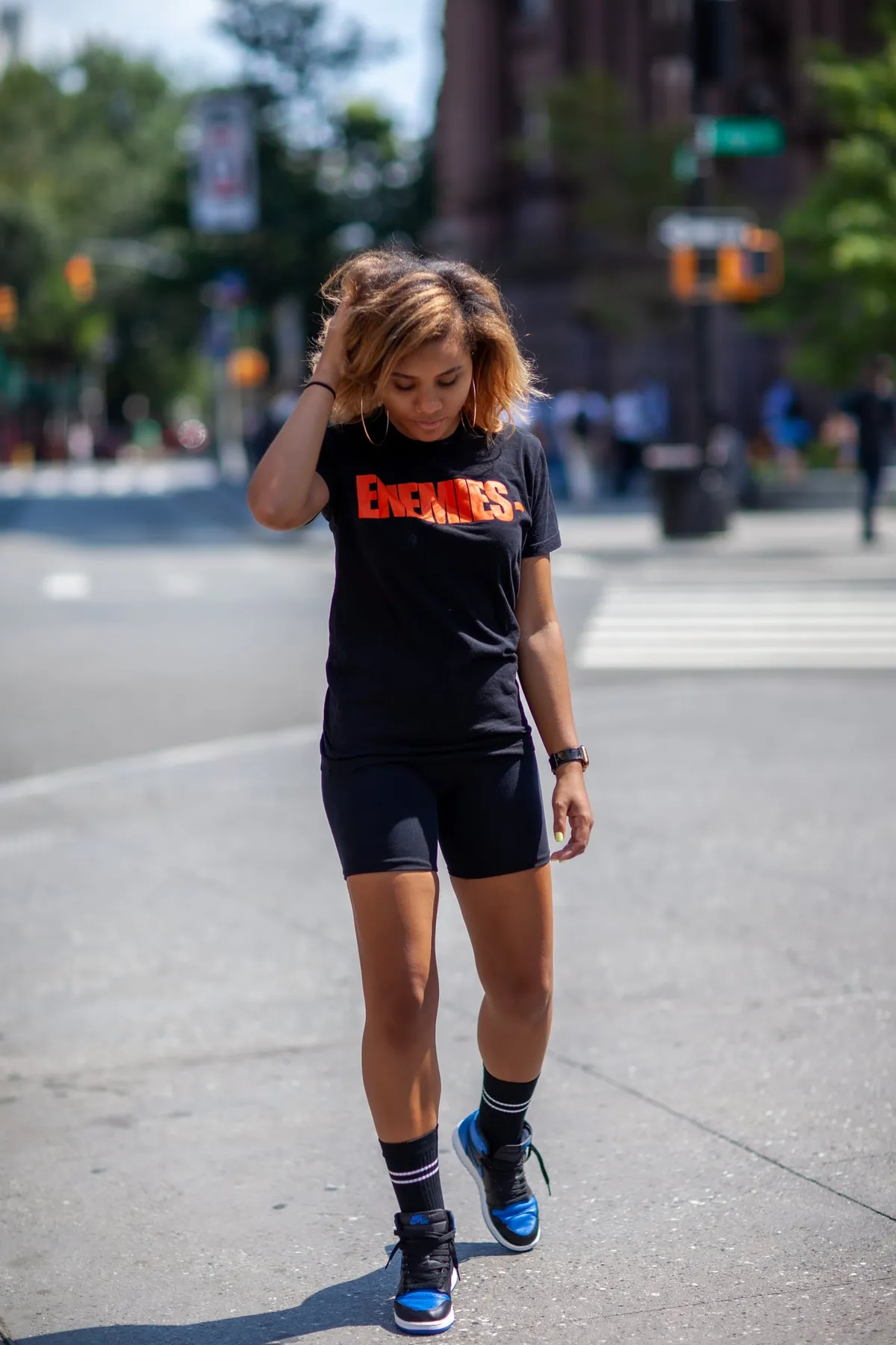 A woman walks across a city intersection, brushing her hair back