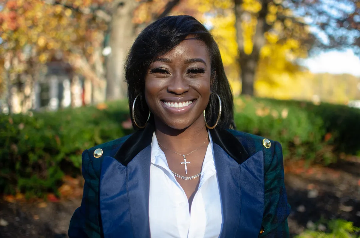 A woman in a navy blazer smiles in golden autumn light