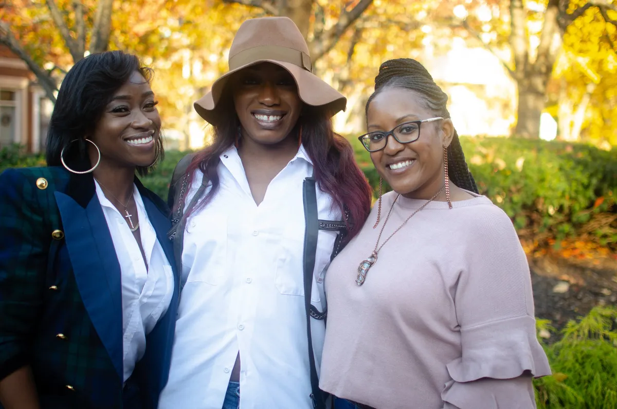 Three women smile together outdoors among autumn trees