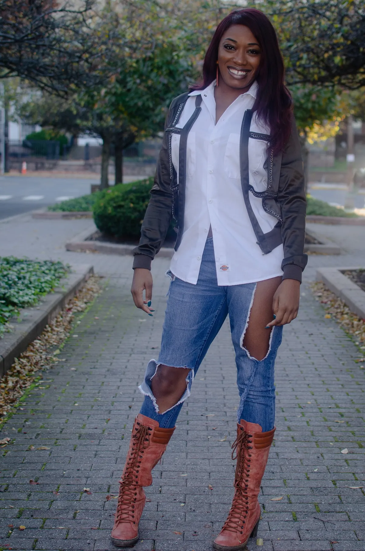 A woman in ripped jeans and tall lace-up boots stands on a garden path