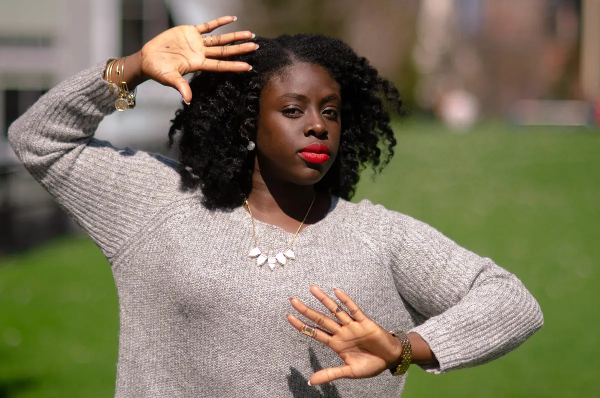 A woman in a grey sweater frames her face with her hands against a green lawn