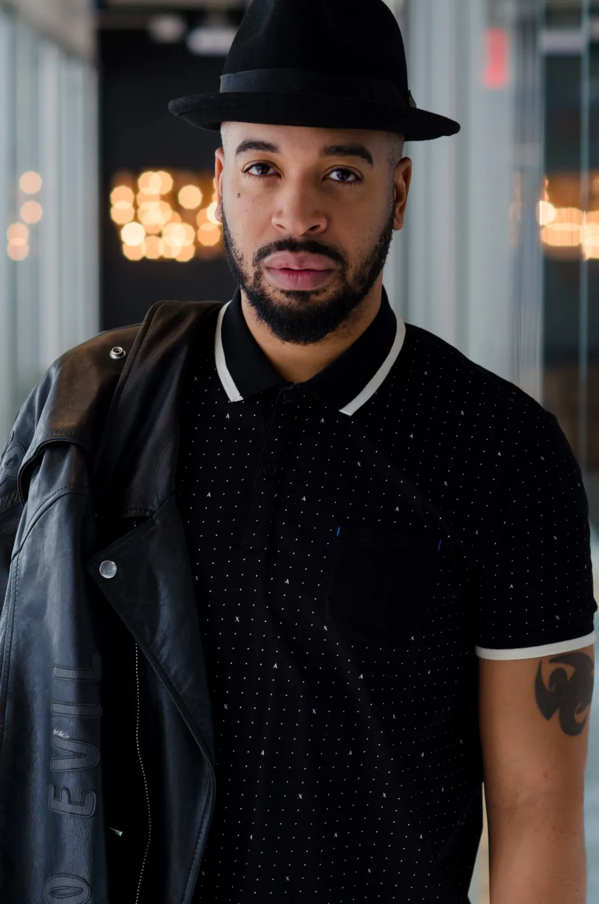 Portrait of a man in a black fedora, polka-dot polo and leather jacket