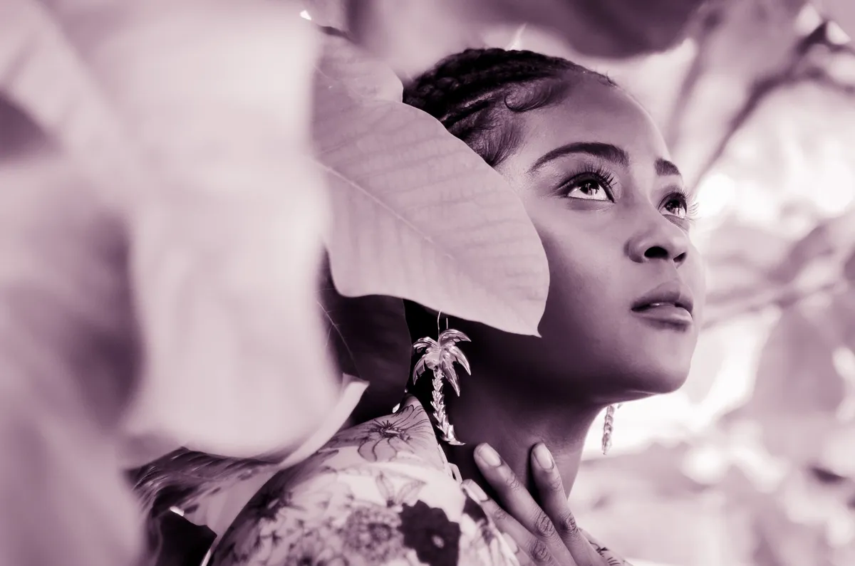 Black-and-white portrait of a woman gazing upward among leaves, wearing statement earrings