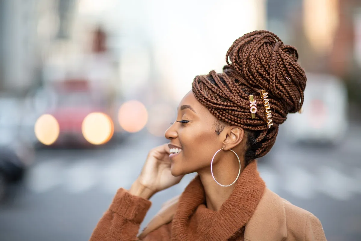 Profile of a woman laughing with her hand at her cheek, gold hoops and a braided bun