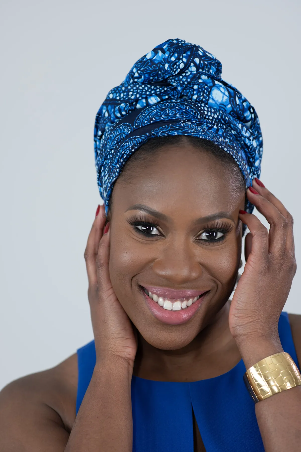 Studio portrait of a smiling woman in a blue patterned head wrap and gold cuff