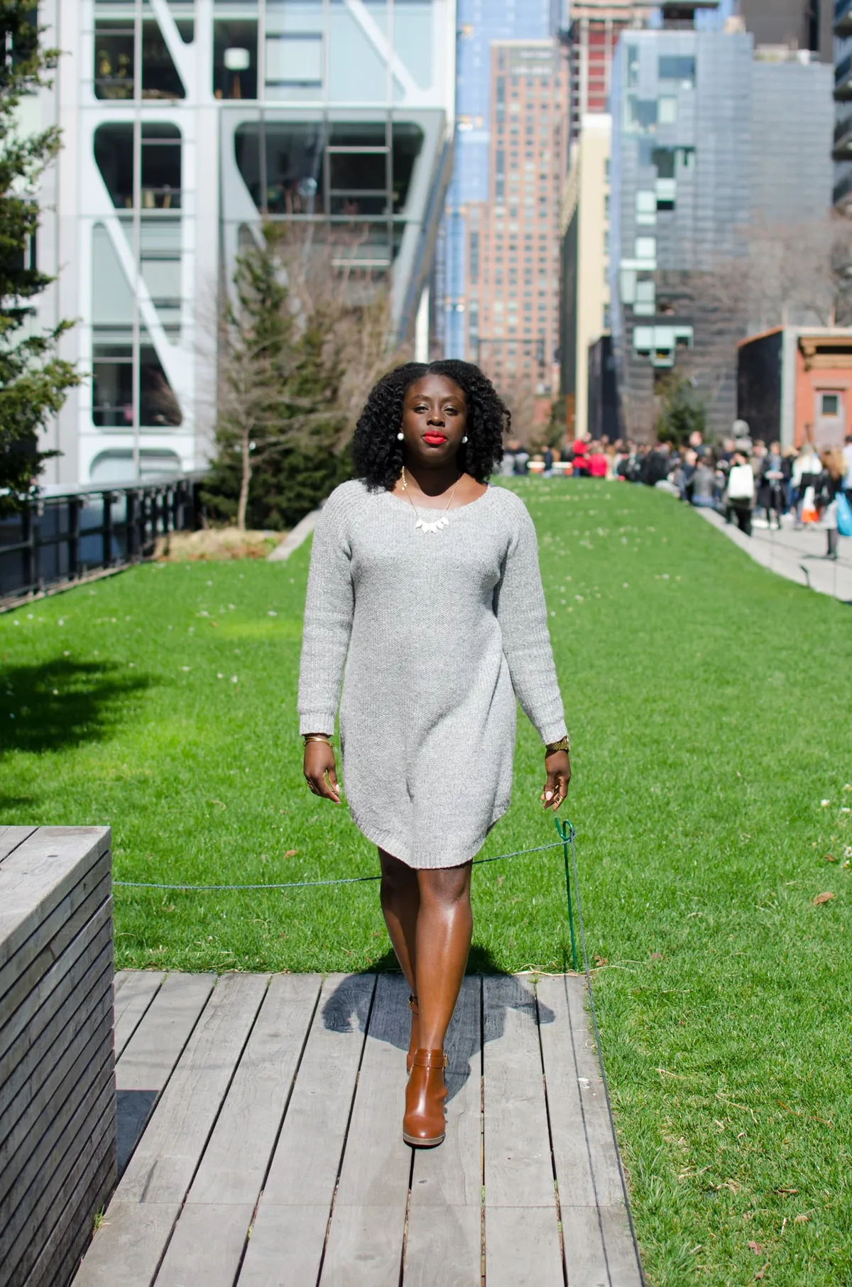 A woman walks toward the camera along a High Line boardwalk with the city skyline behind her