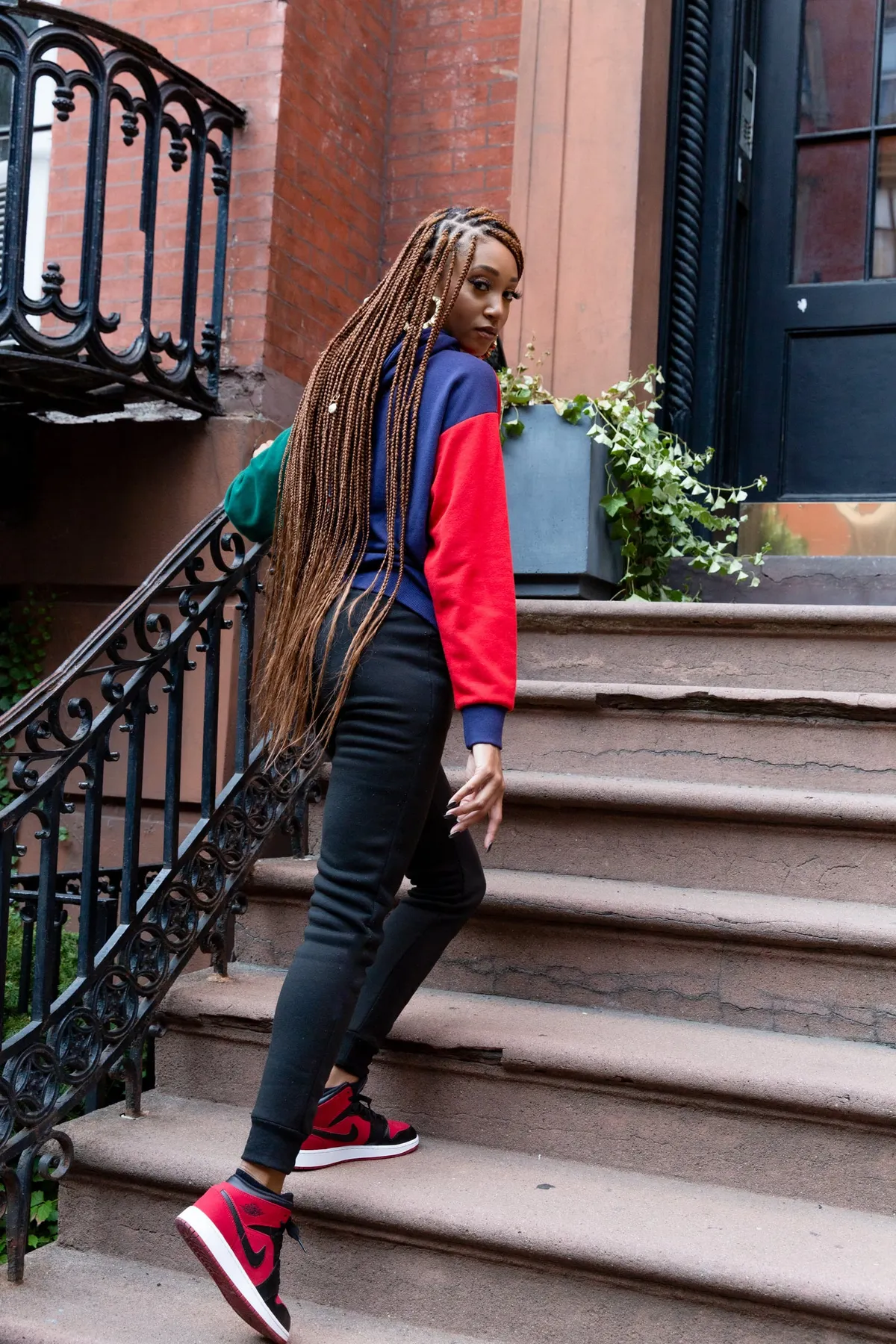 A woman glances back over her shoulder while climbing a brownstone stoop with wrought iron railings